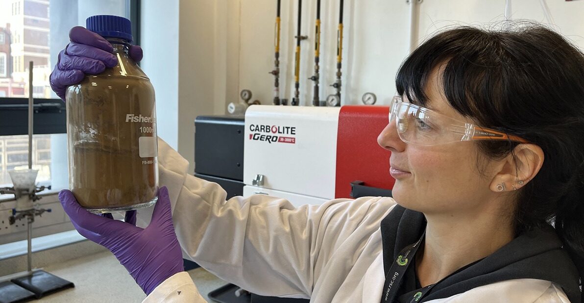 woman in white coat working in laboratory looking at contents of a bottle